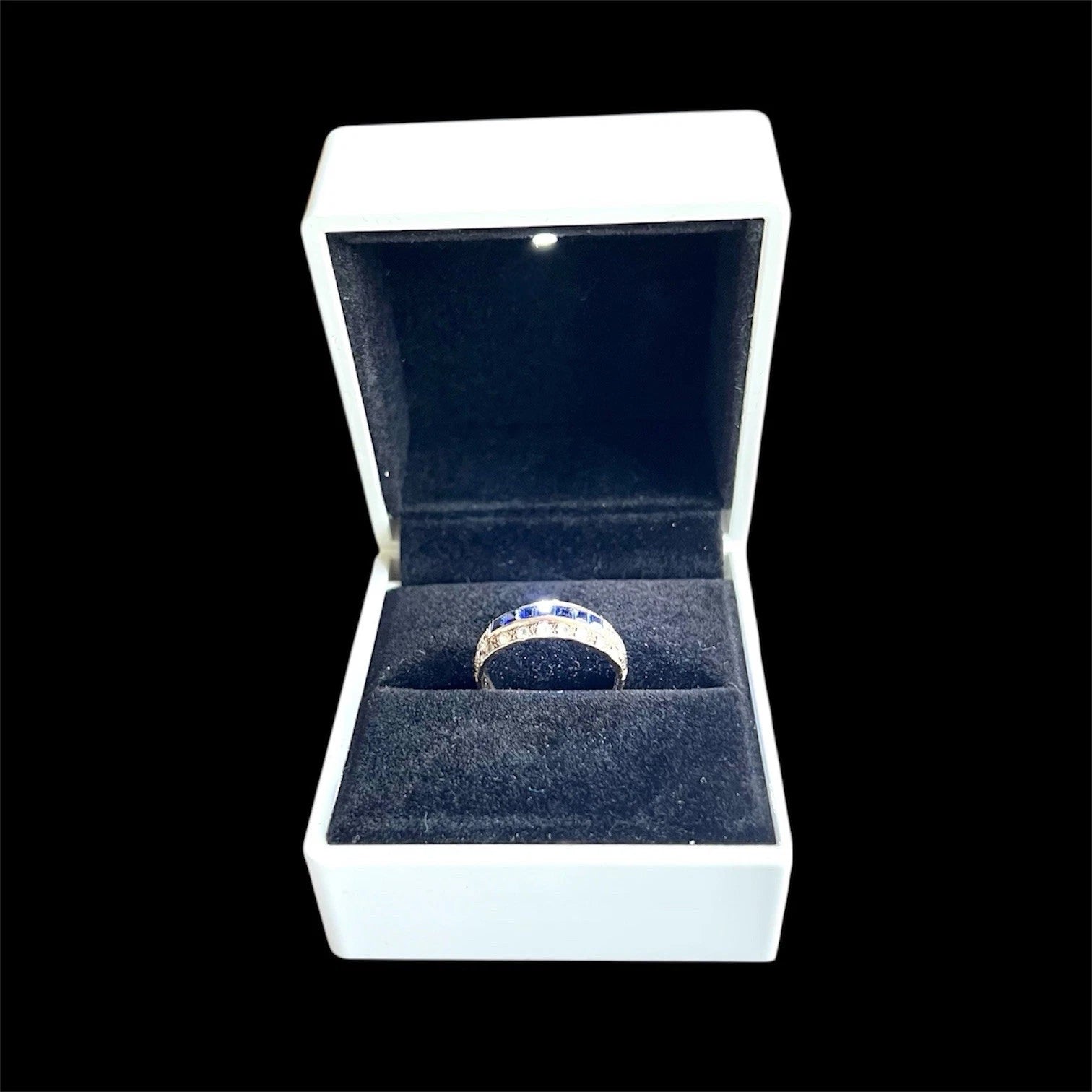 Gold ring with blue sapphire gemstones in an open white box on a black background