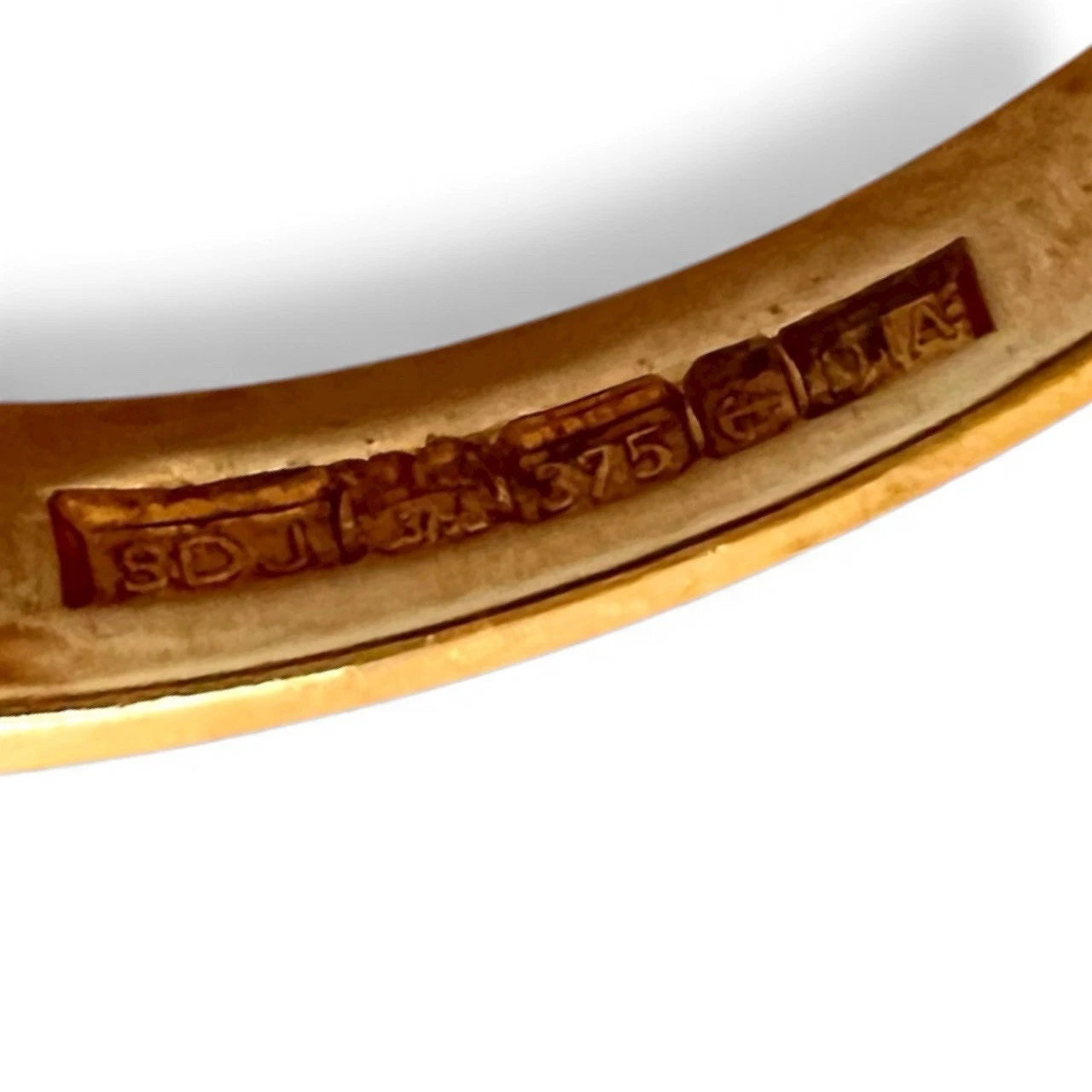 Close-up of a gold ring with engraved hallmark on a white background