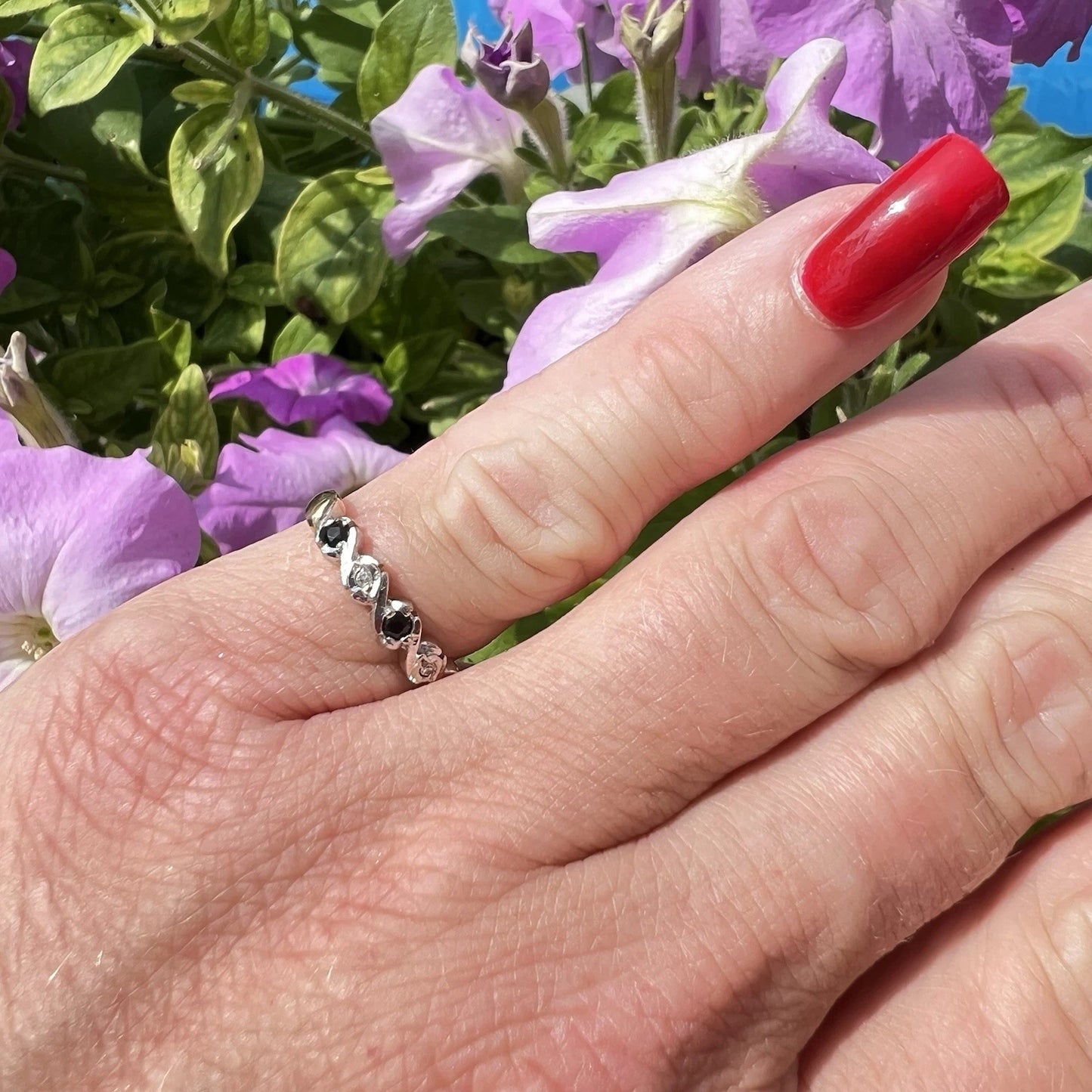 Hand wearing a gold ring with black stones against a background of purple flowers