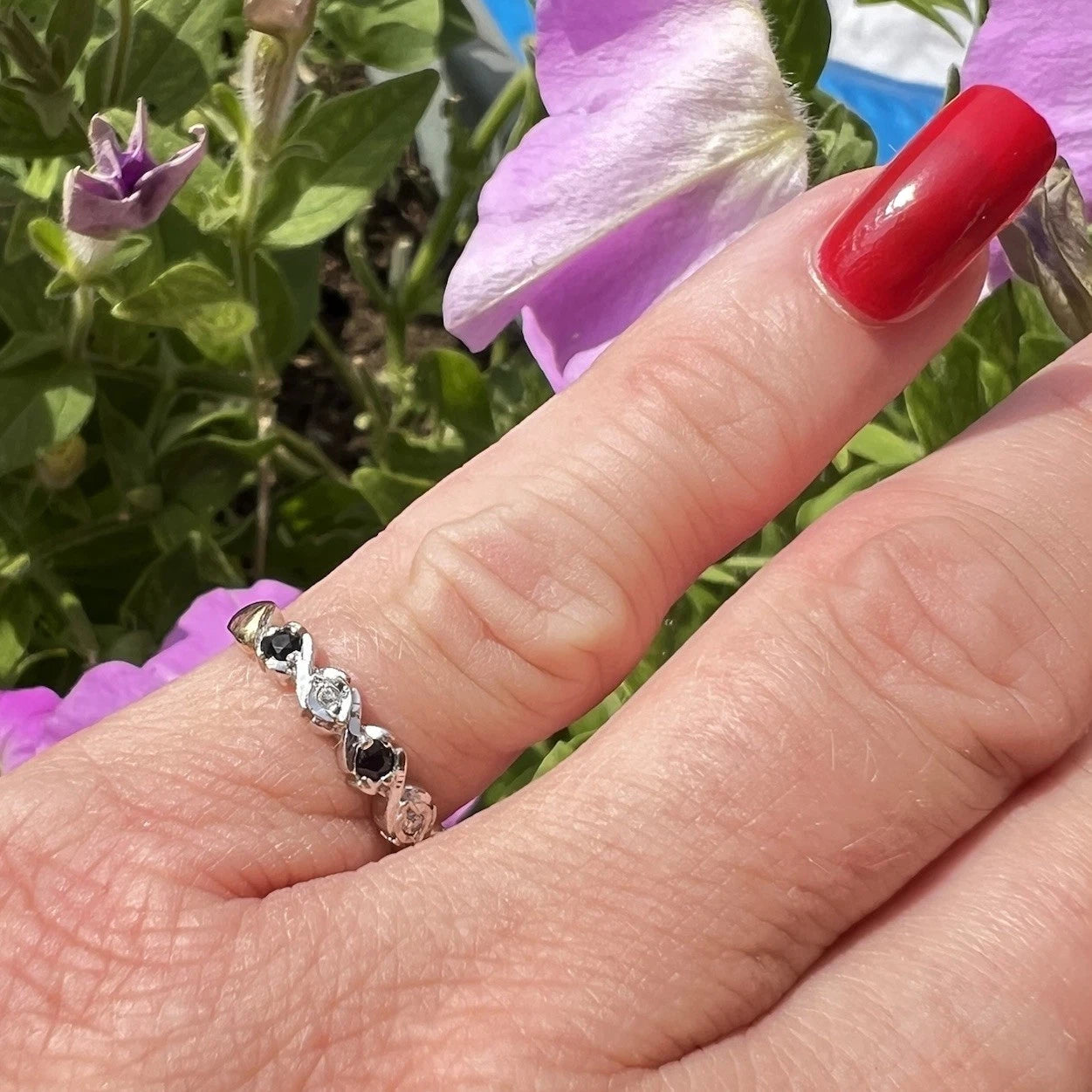 Hand wearing a ring with sapphire and diamond gemstones in front of purple flowers