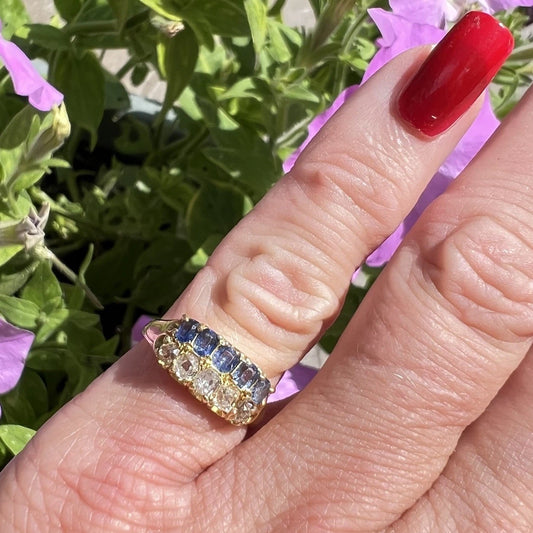 Hand wearing a Victorian gold ring with sapphire and diamond gemstones against a floral background