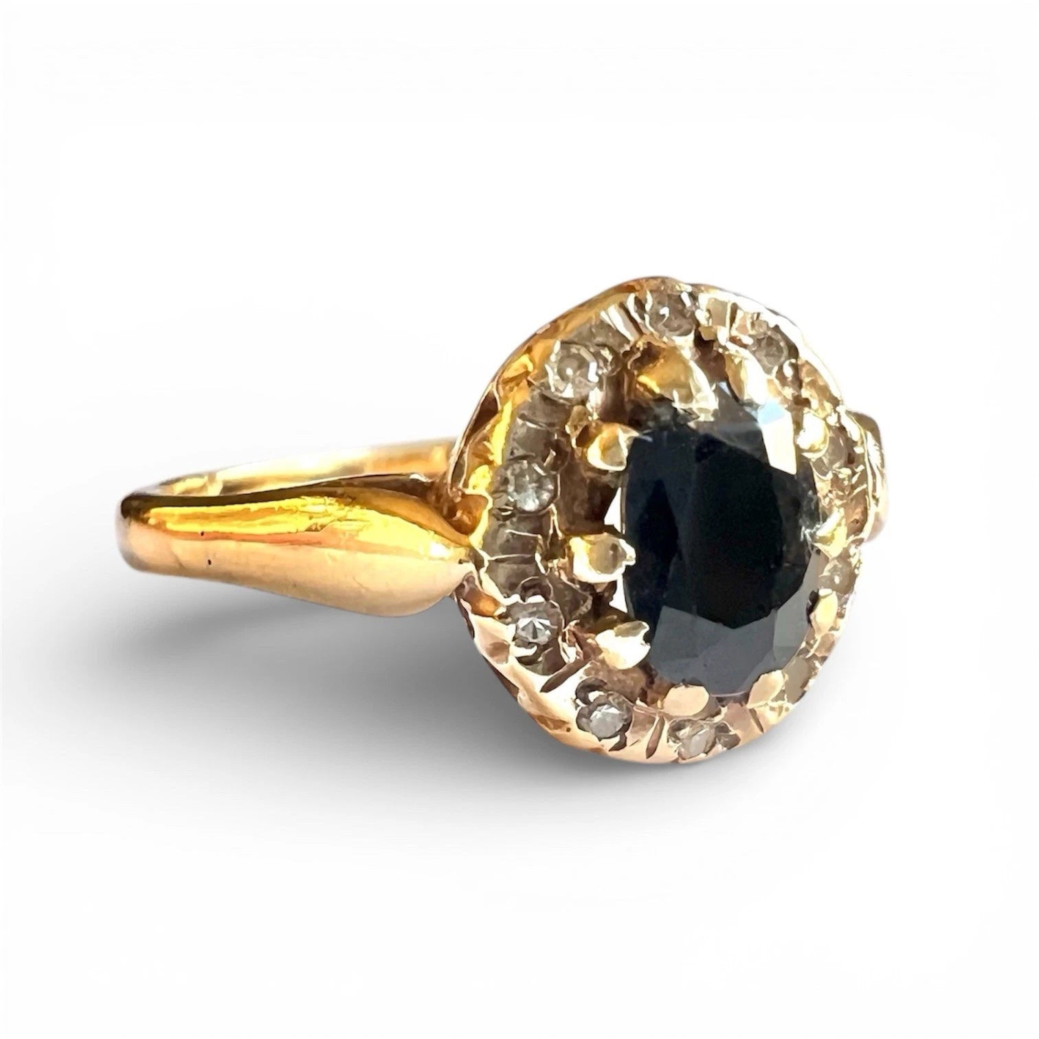 Gold ring with a sapphire gemstone and diamond surround on a white background