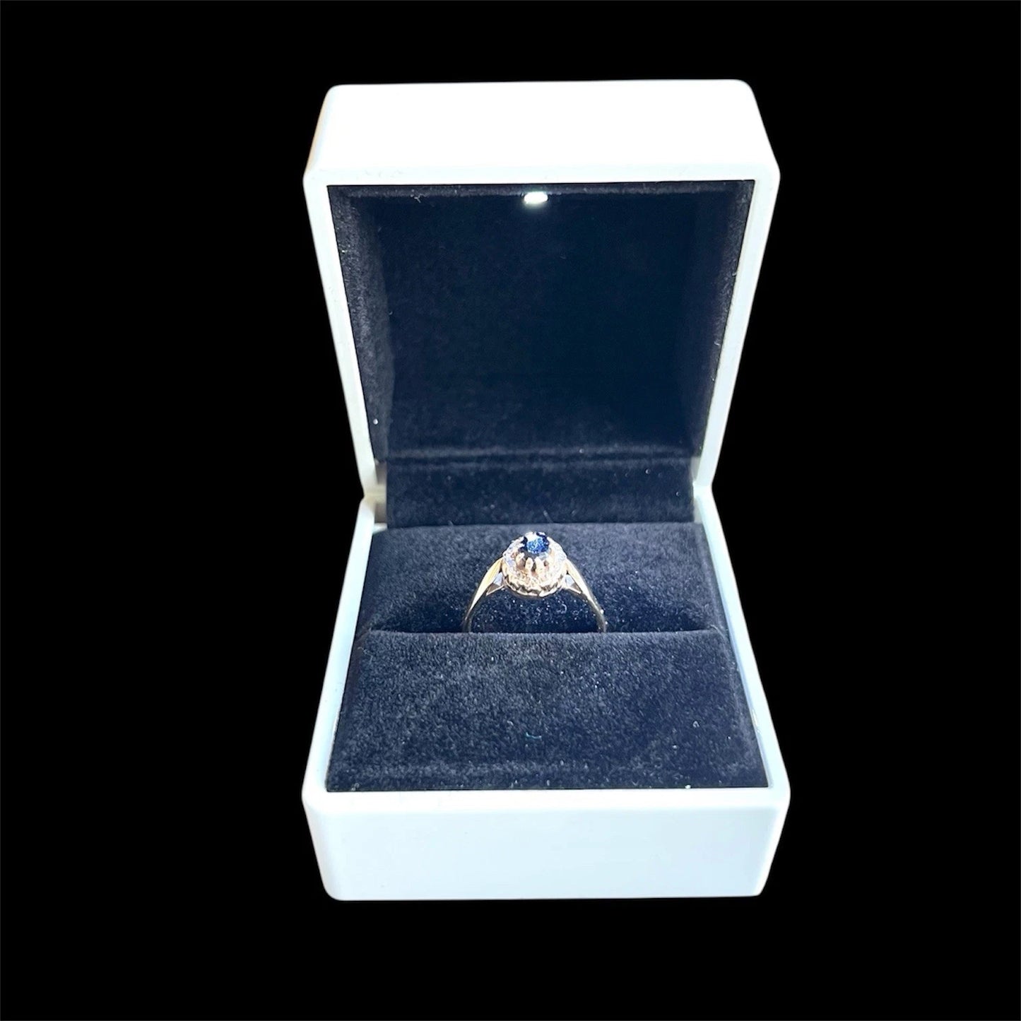 Sapphire and diamond halo ring in a white box with a black background