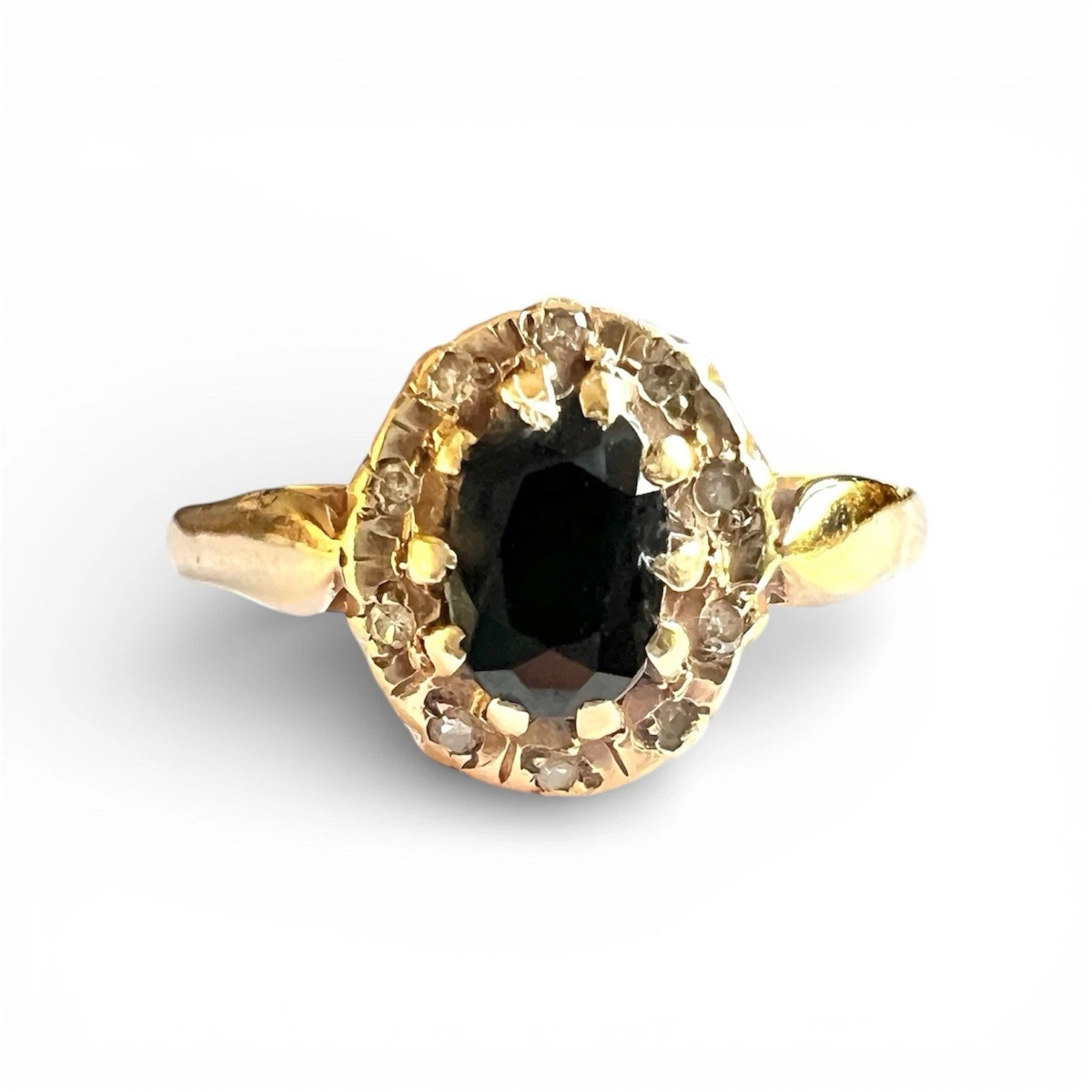 Gold ring with a sapphire gemstone and diamond surround on a white background