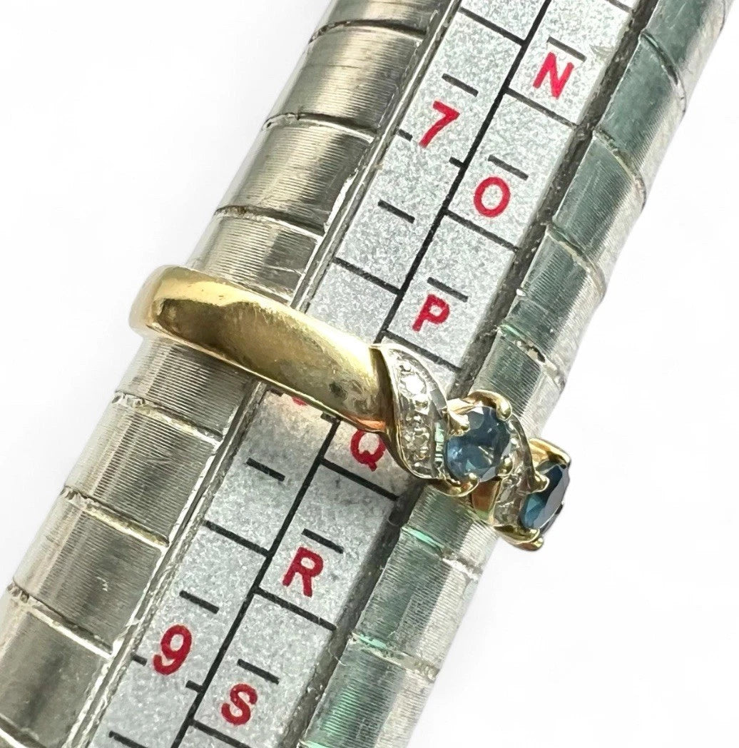 Gold ring with a blue gemstone on a metal ring sizer for size reference