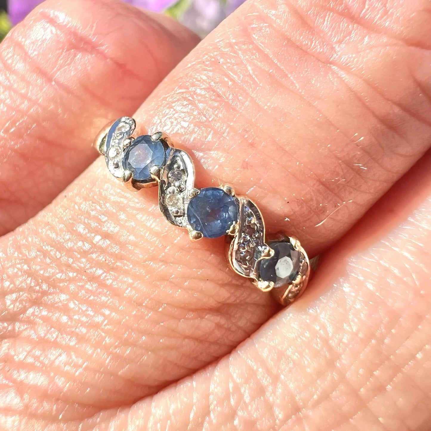 Gold ring with light blue sapphire gemstones and diamond on a person's finger