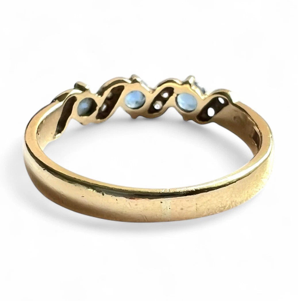 Gold ring with three light blue sapphire gemstones on a white background. Rear view close up of setting and gold band. 