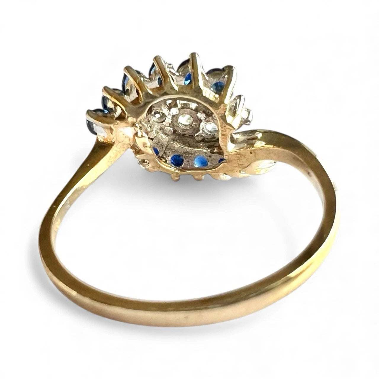 Gold cluster ring with blue sapphire gemstones and diamonds on a white background close up rear view of setting and gold band 