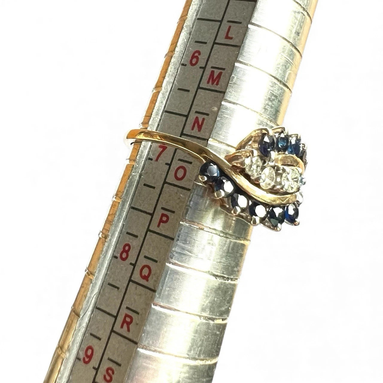 Gold ring with sapphire gemstones and diamonds on a ruler for size reference