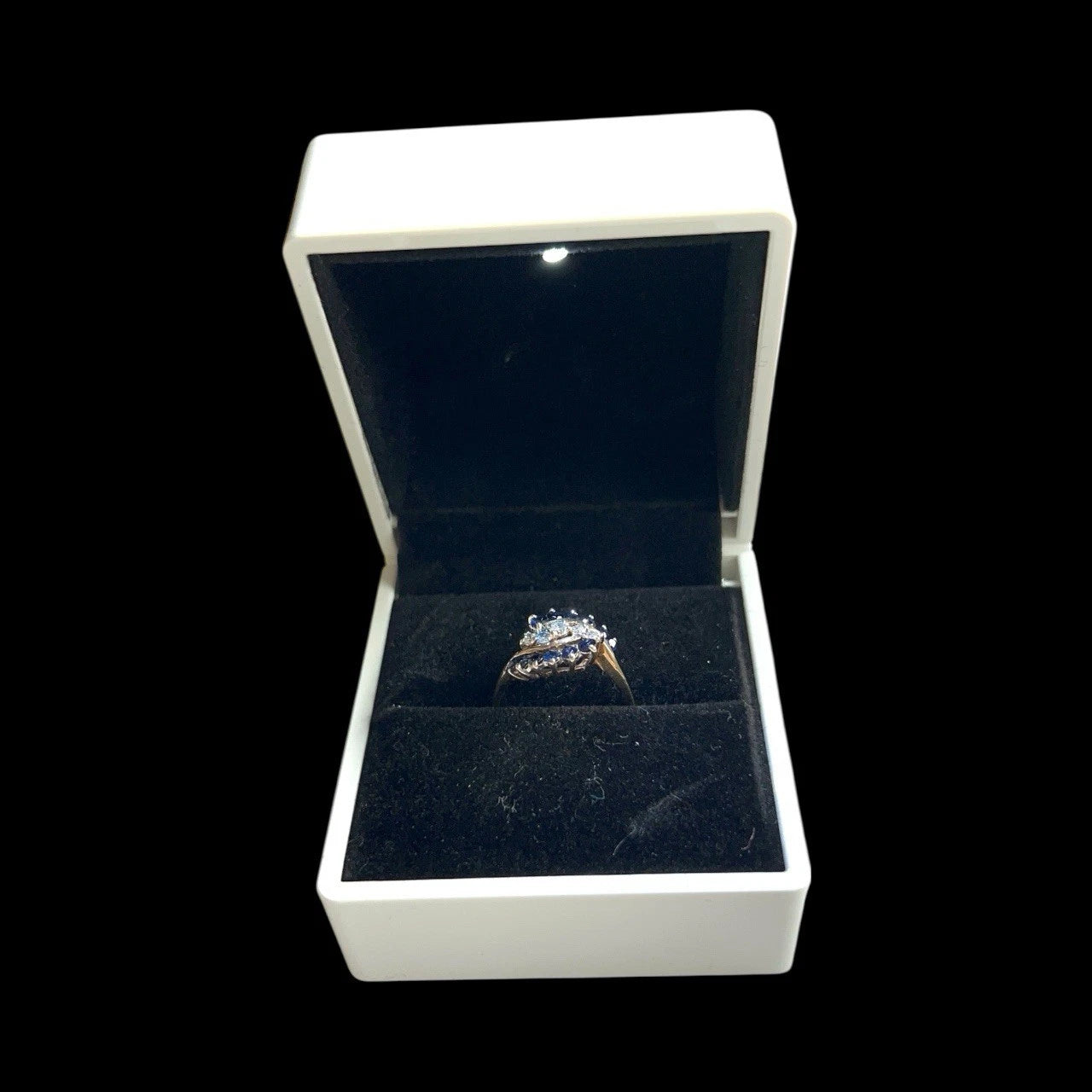 Diamond and sapphire cluster ring in a white box with a black interior