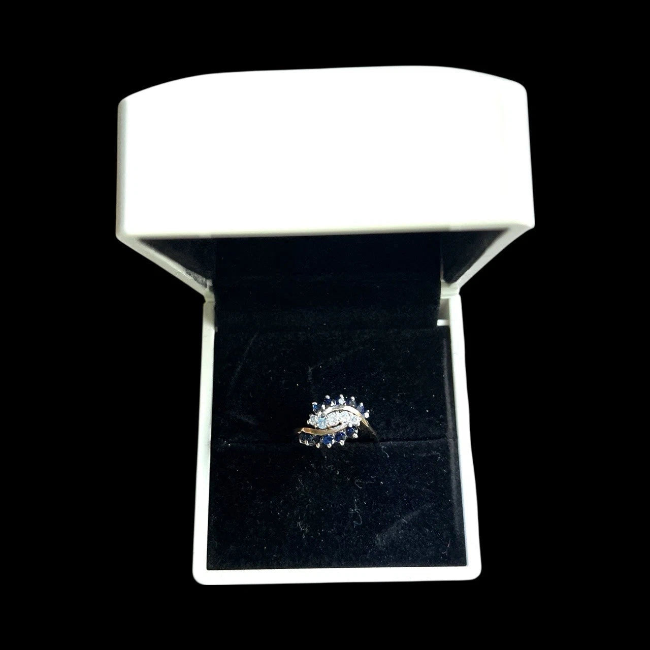 Gold ring with sapphire and diamond gemstones in a white box on a black background