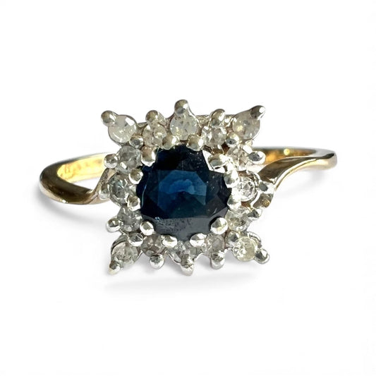 Gold ring with a blue sapphire gemstone and diamond halo on a white background