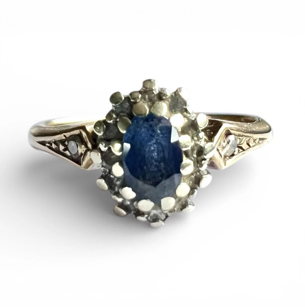 Gold ring with a blue sapphire gemstone and diamond halo on a white background
