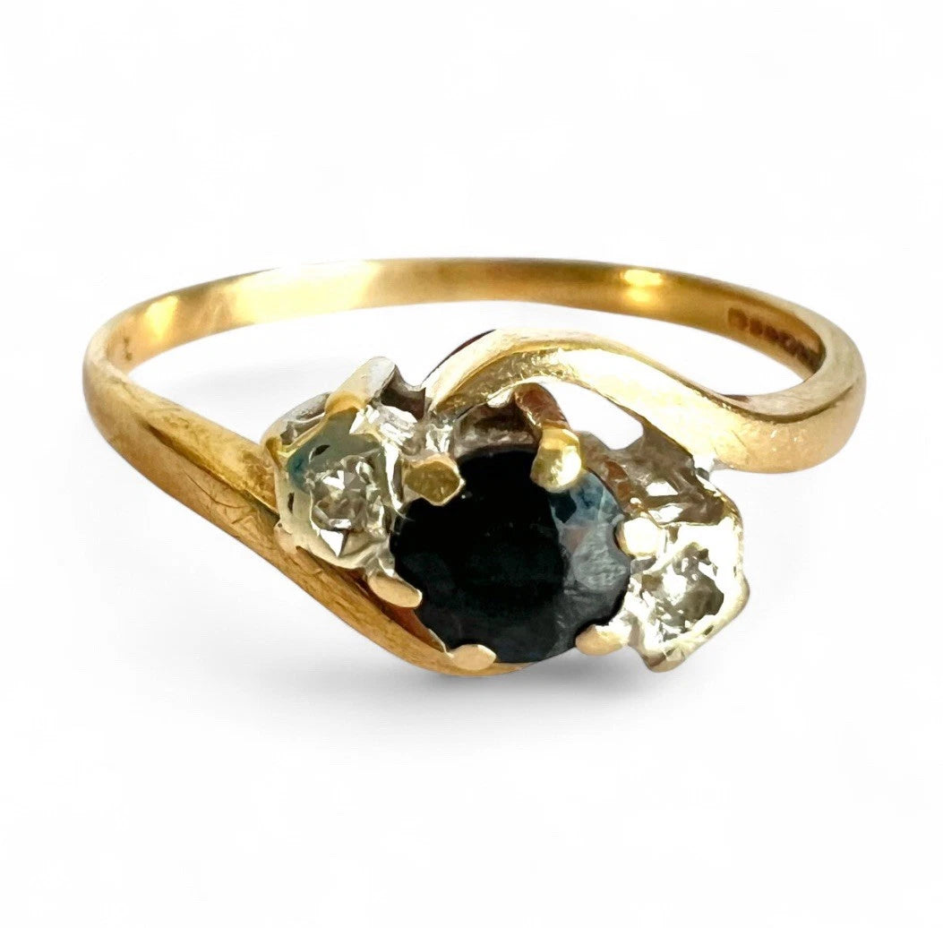 Three stone gold ring with a central sapphire gemstone and two smaller diamonds on a white background