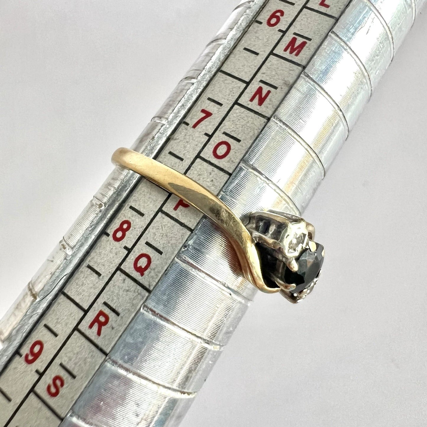 Gold ring with a sapphire and diamonds on a metal ruler for size reference