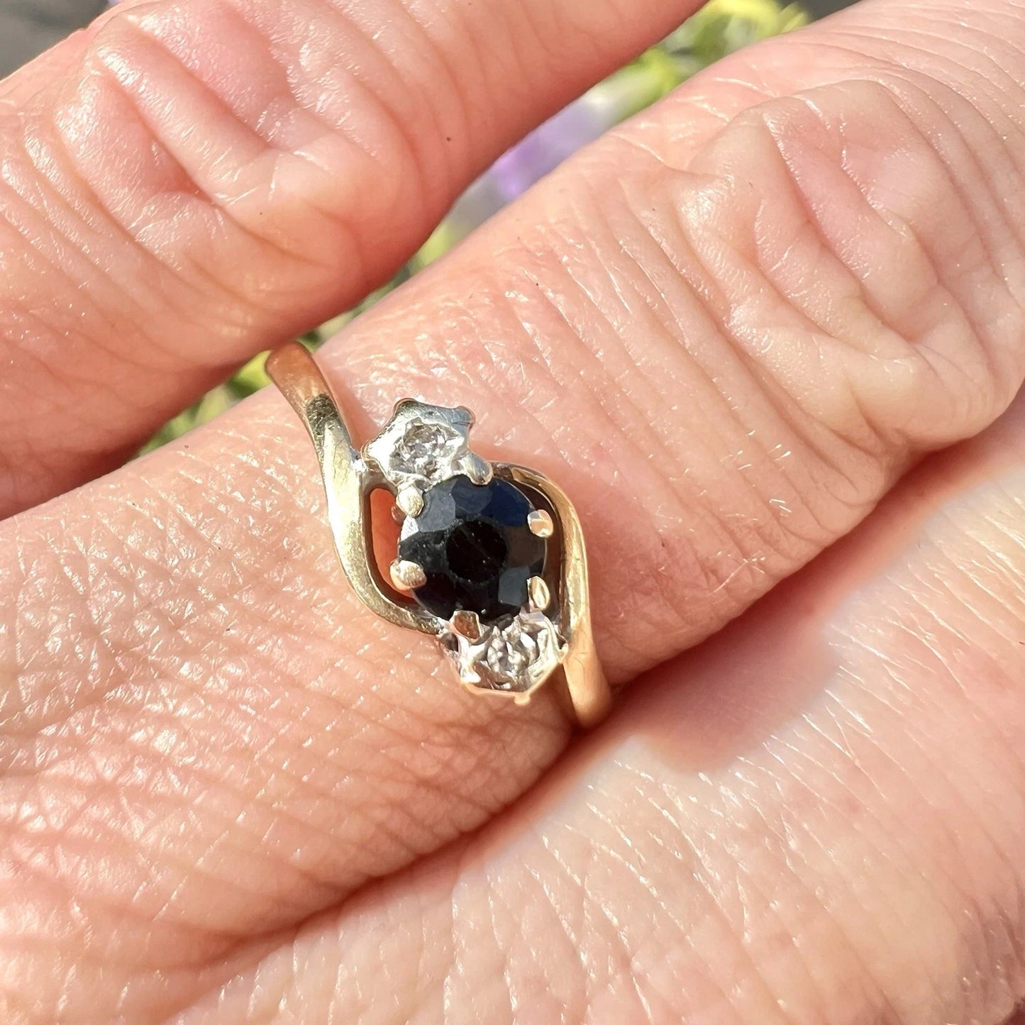 Gold ring with a central blue sapphire gemstone and smaller diamonds on a finger.