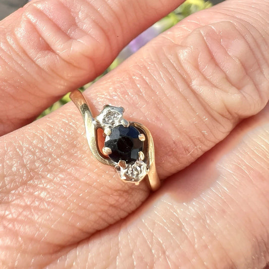 Gold ring with a central blue sapphire gemstone and smaller diamonds on a finger.