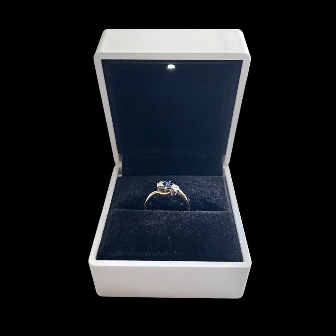 Gold ring with a blue sapphire gemstone in an open jewellery box on a black background