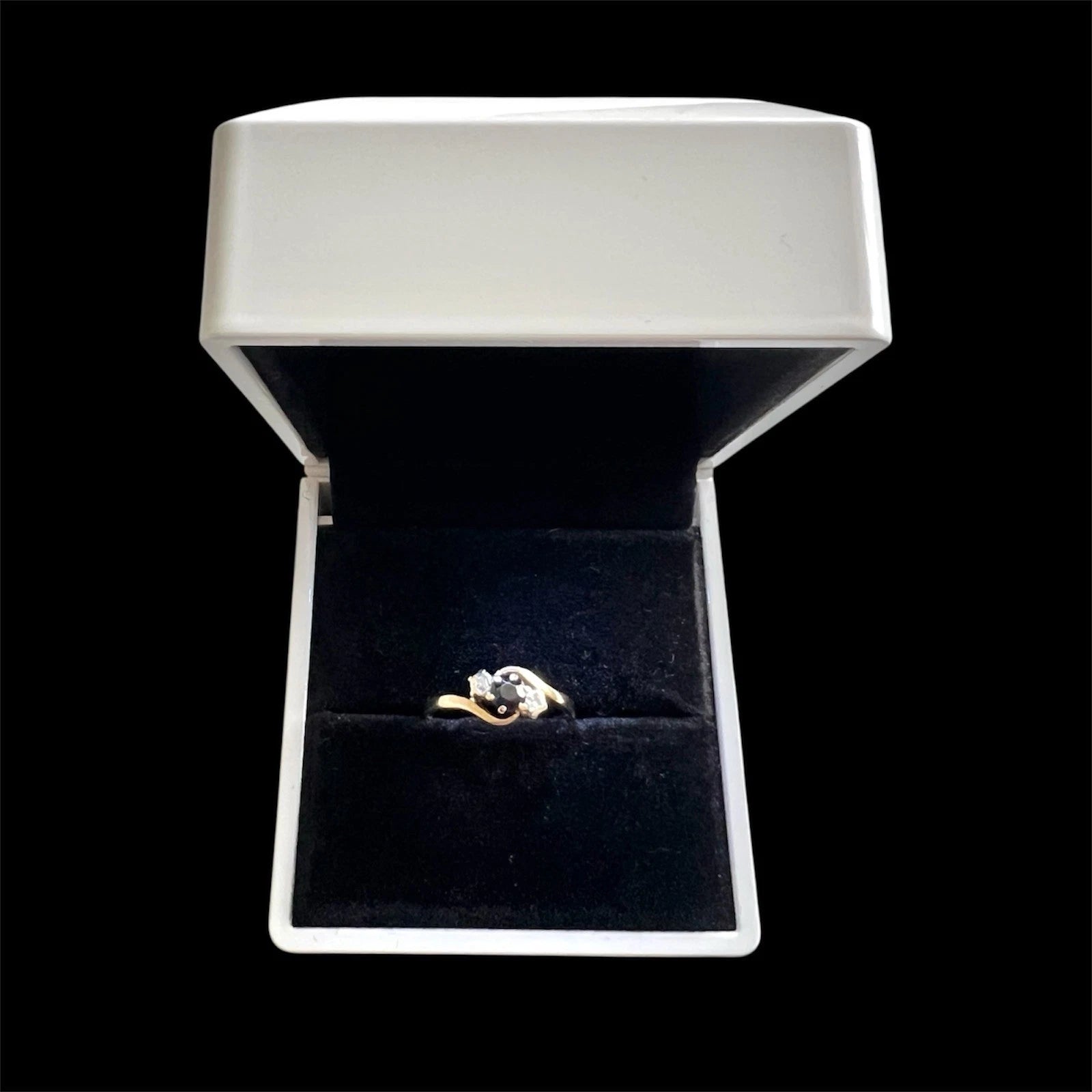 Gold ring with a sapphire and diamond in a white jewellery box on a white stand against a black background