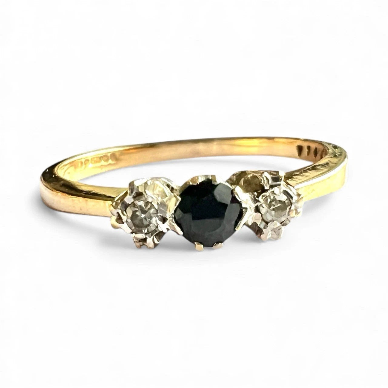 Gold ring with a central sapphire gemstone flanked by two smaller diamonds on a white background