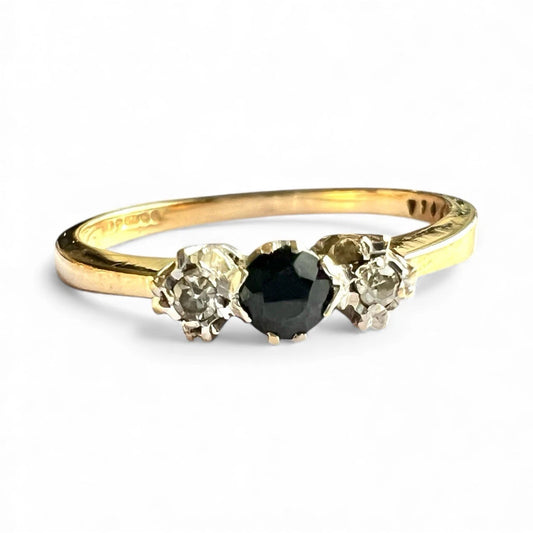 Gold ring with a central sapphire gemstone flanked by two smaller diamonds on a white background