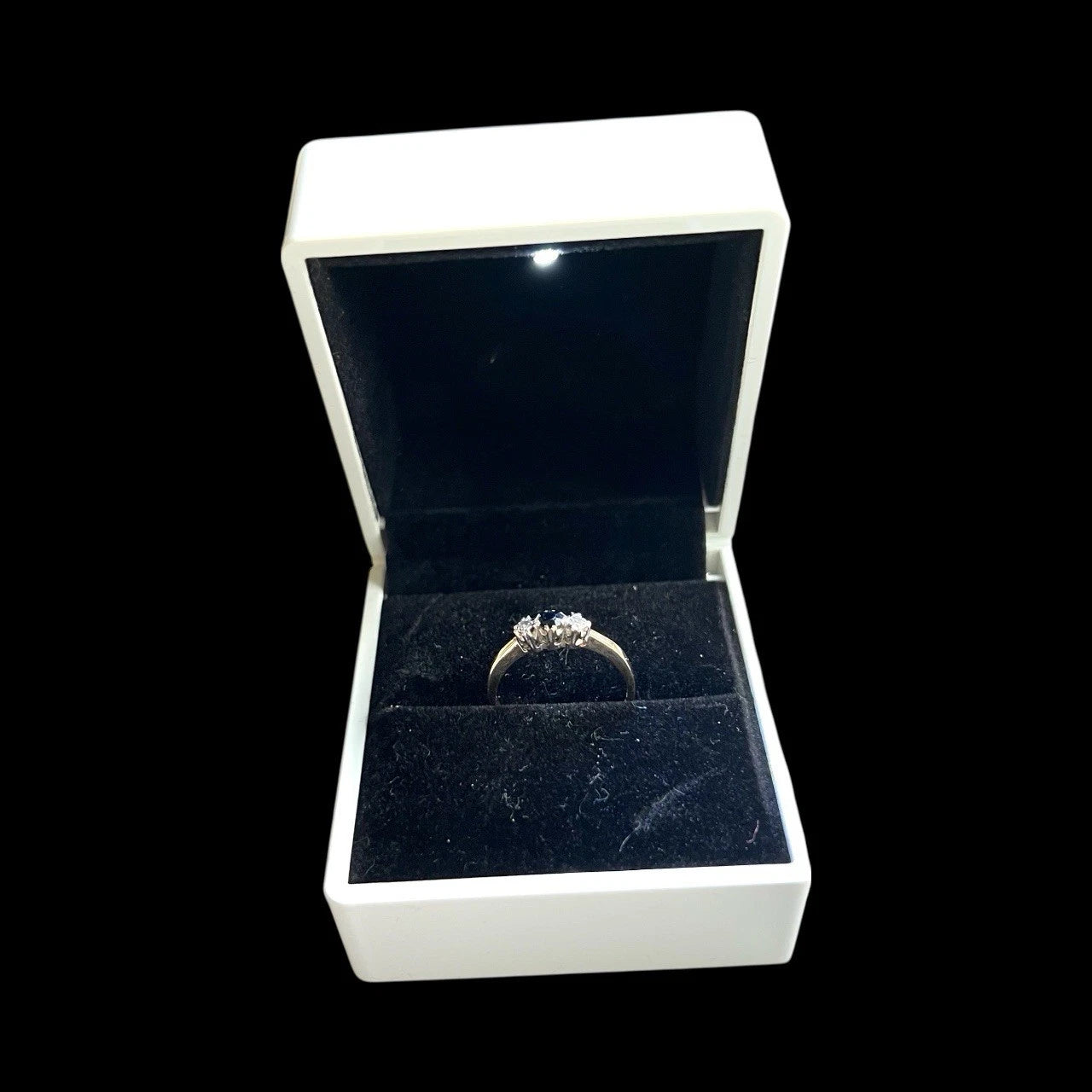 Gold sapphire and diamond three stone ring in an open jewellery box on a black background