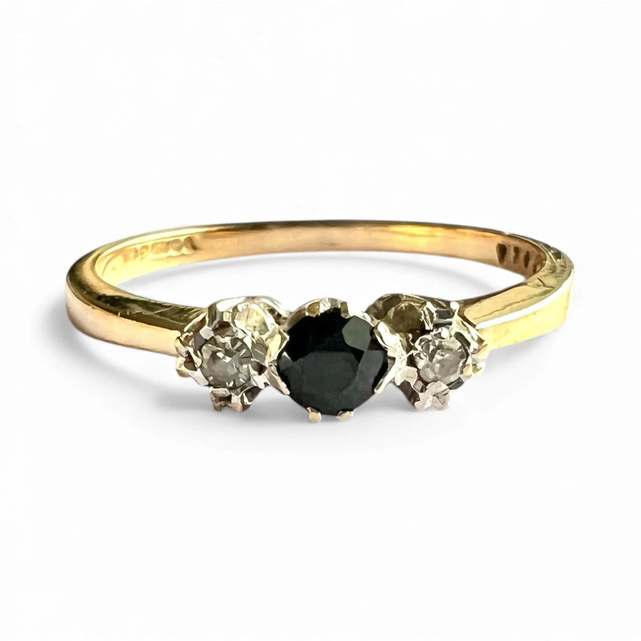 Gold ring with a central sapphire gemstone flanked by two smaller diamonds on a white background