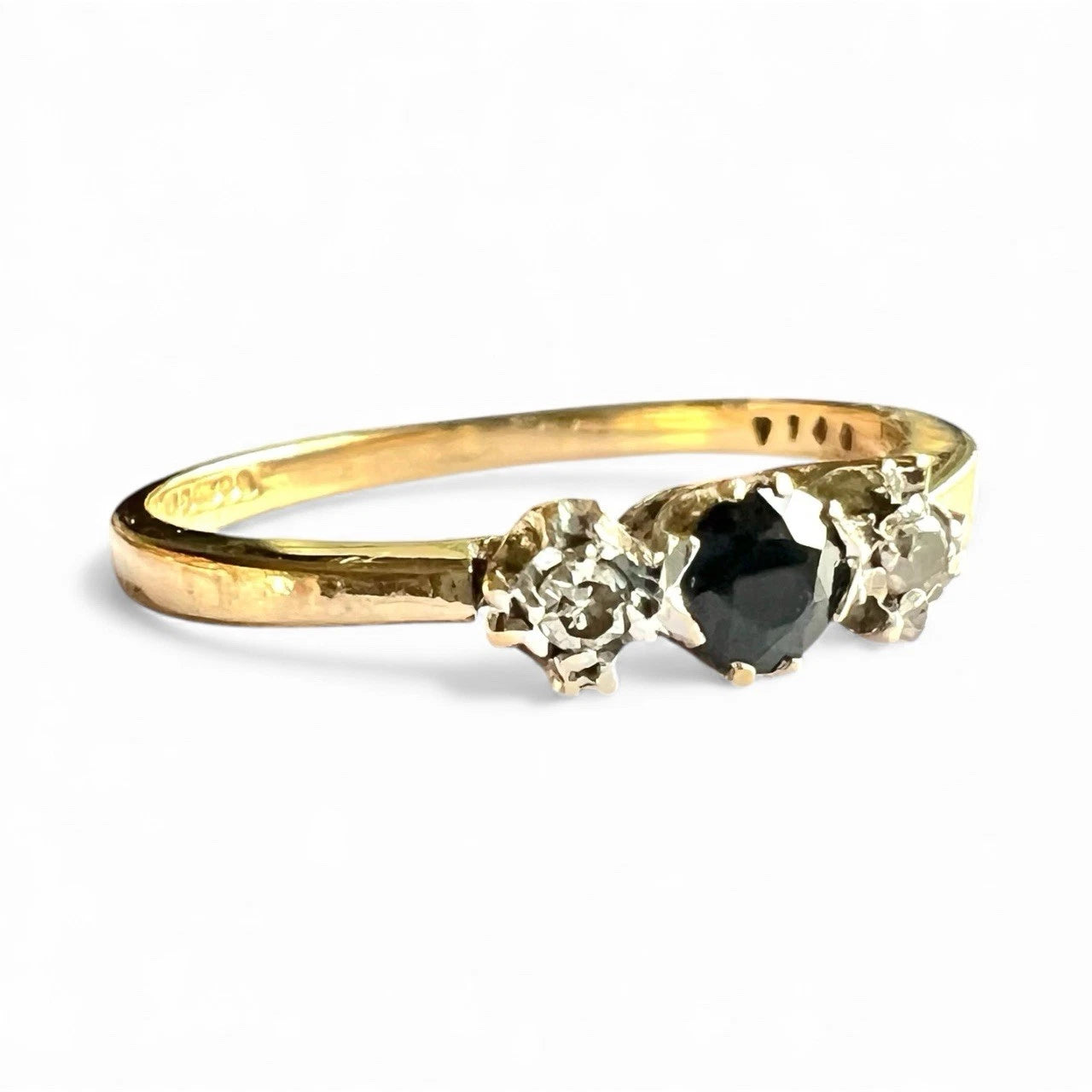 Three stone gold ring with a sapphire and smaller diamonds on a white background