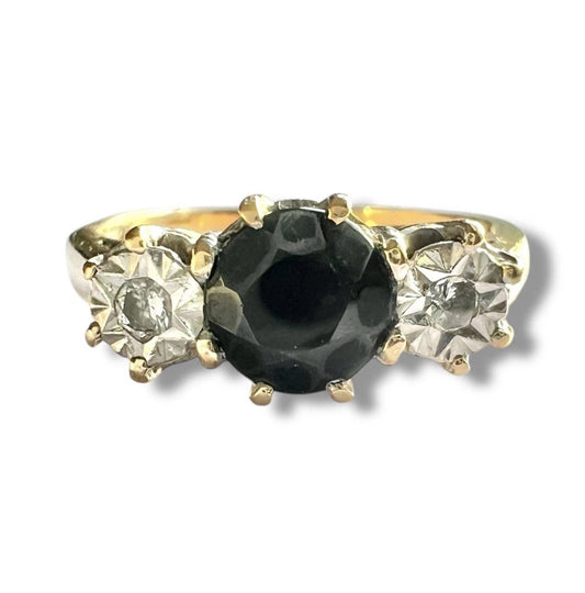Gold ring with a central sapphire gemstone and two diamonds on a white background, close-up front view of setting 
