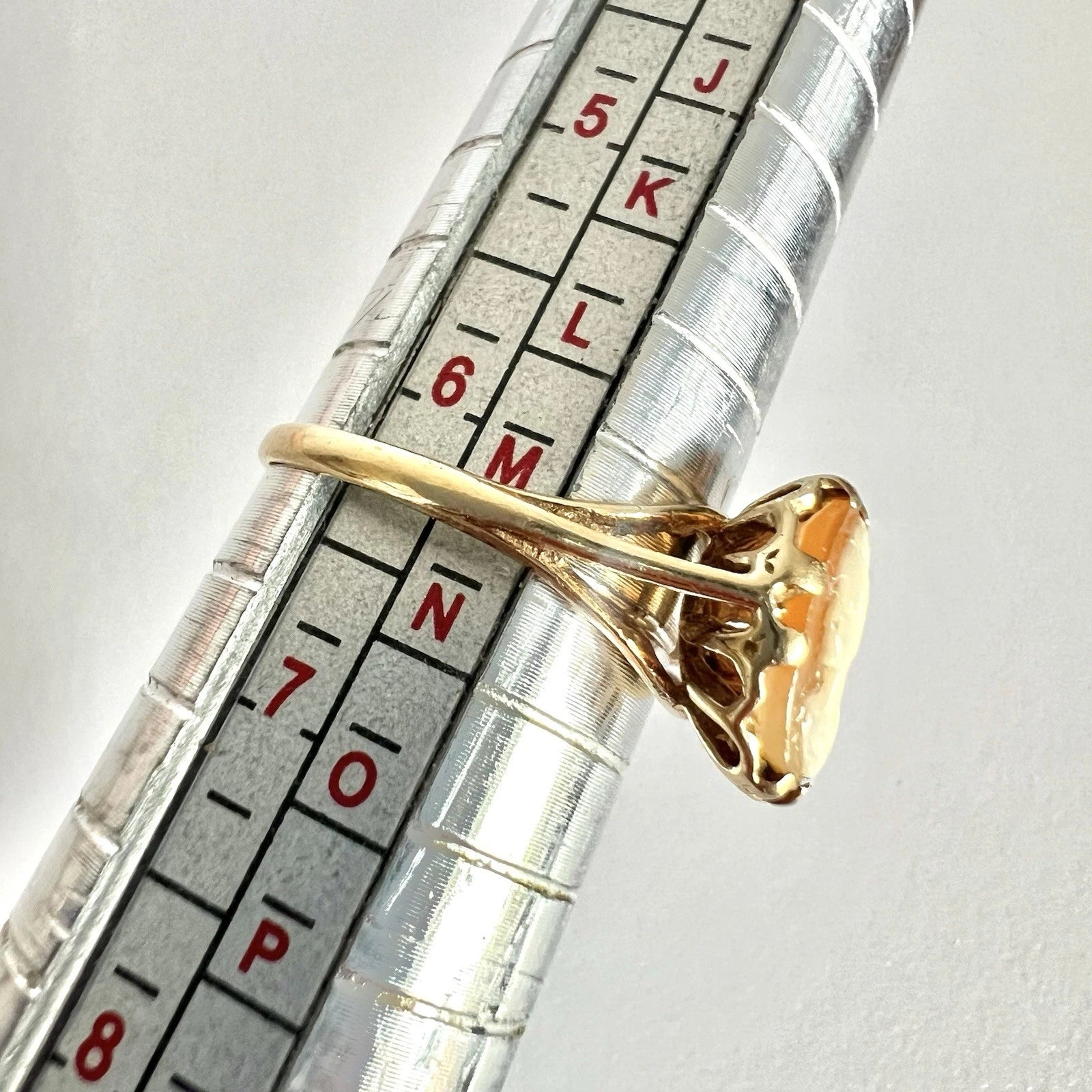 Gold ring on a ruler for size reference against a white background