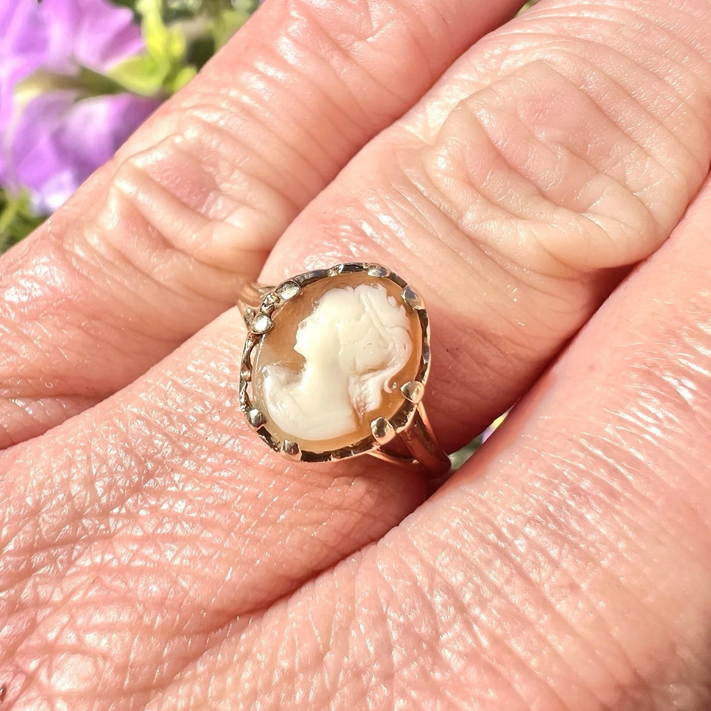 Vintage-style cameo ring on a person's finger with a blurred floral background