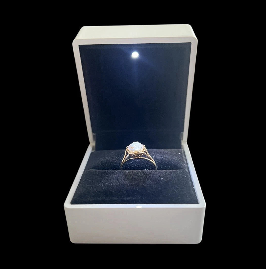 Gold ring in a white box with blue interior on a black background