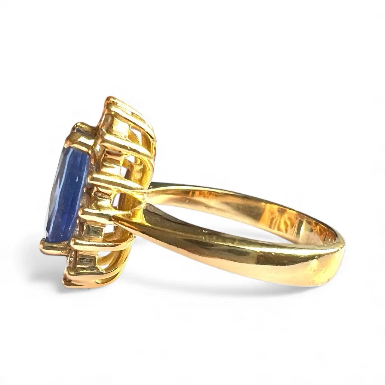 Gold ring with a blue tanzanite gemstone and diamond halo on a white background, close-up side view of gold band and setting 
