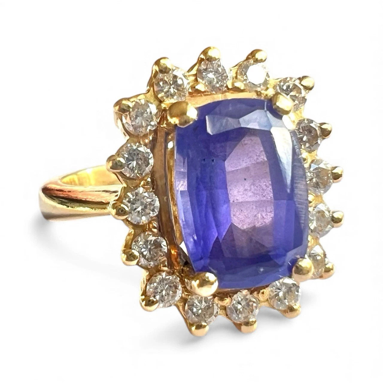 Gold ring with a blue tanzanite gemstone and diamond halo a white background, close up view of setting 