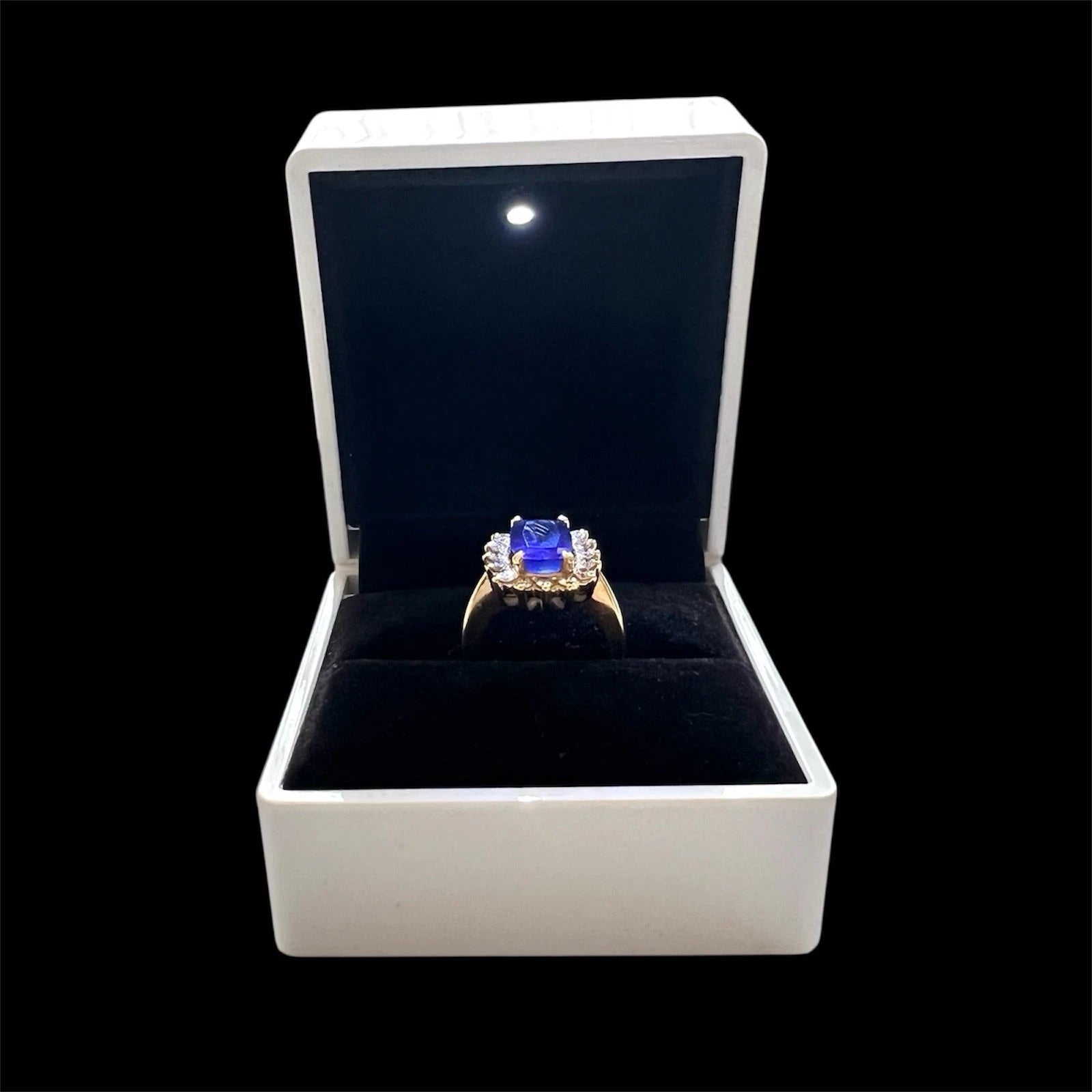 Ring with a large blue tanzanite gemstone and diamond halo in a white box on a black background