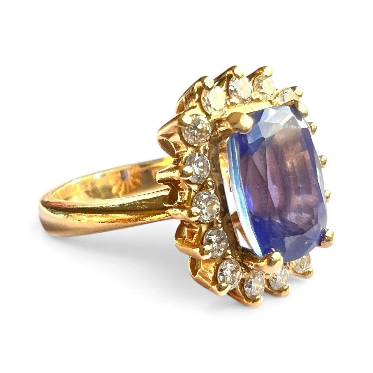 Gold ring with a blue tanzanite gemstone and smaller diamond halo on a white background