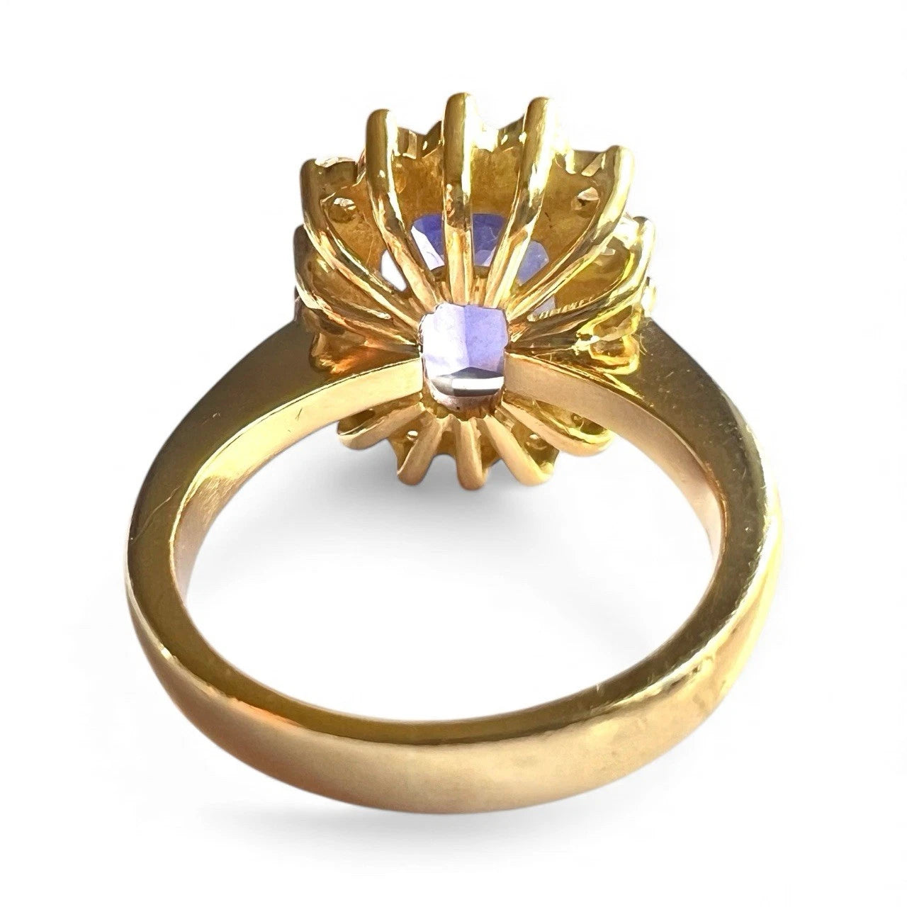 Gold ring with a large blue tanzanite gemstone and diamond halo on a white background, rear view close up of setting and gold band 