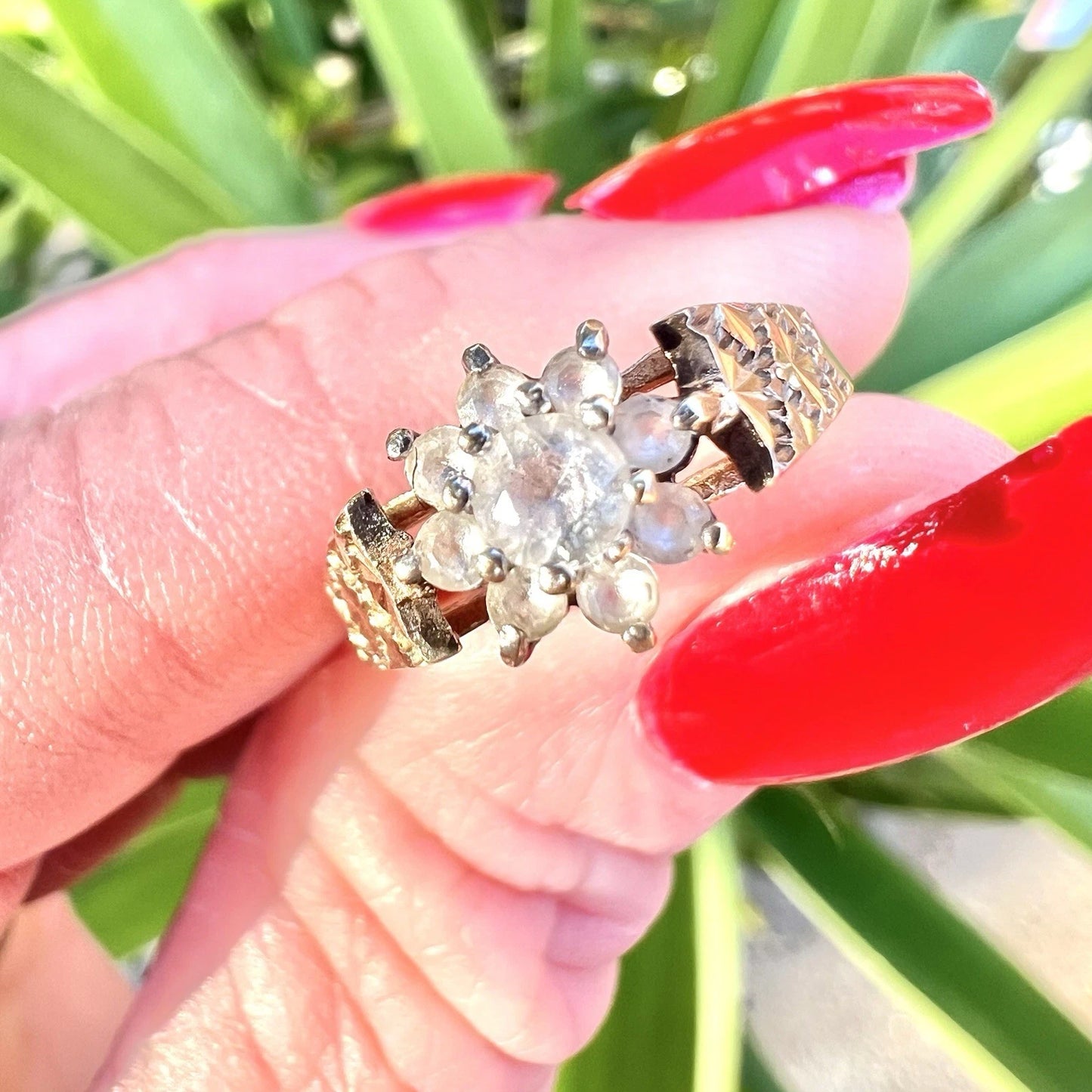 Gold ring with topaz gemstones held by a hand with red nail polish against a green leafy background