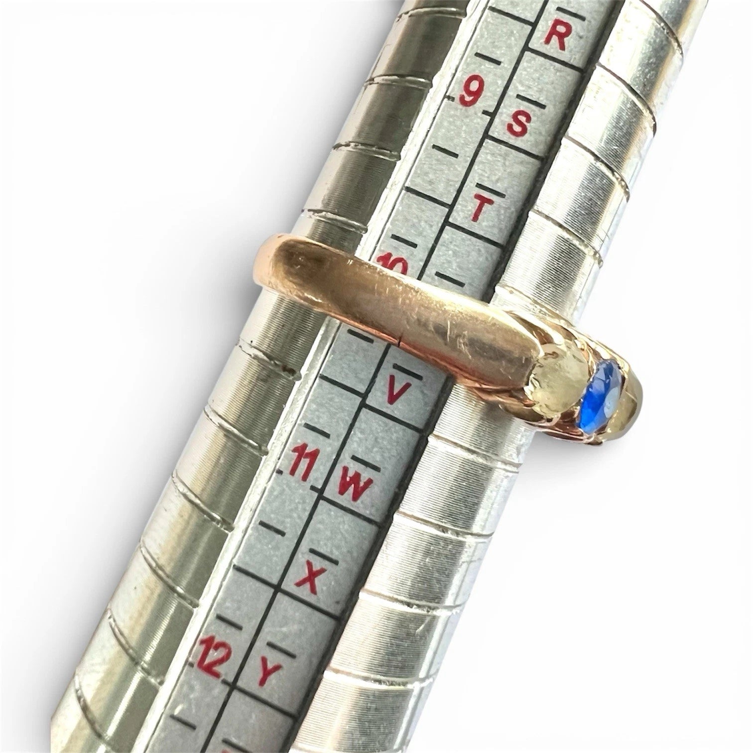 Close-up of a measuring tool with a gold antique ring with blue and clear gemstones on a white background