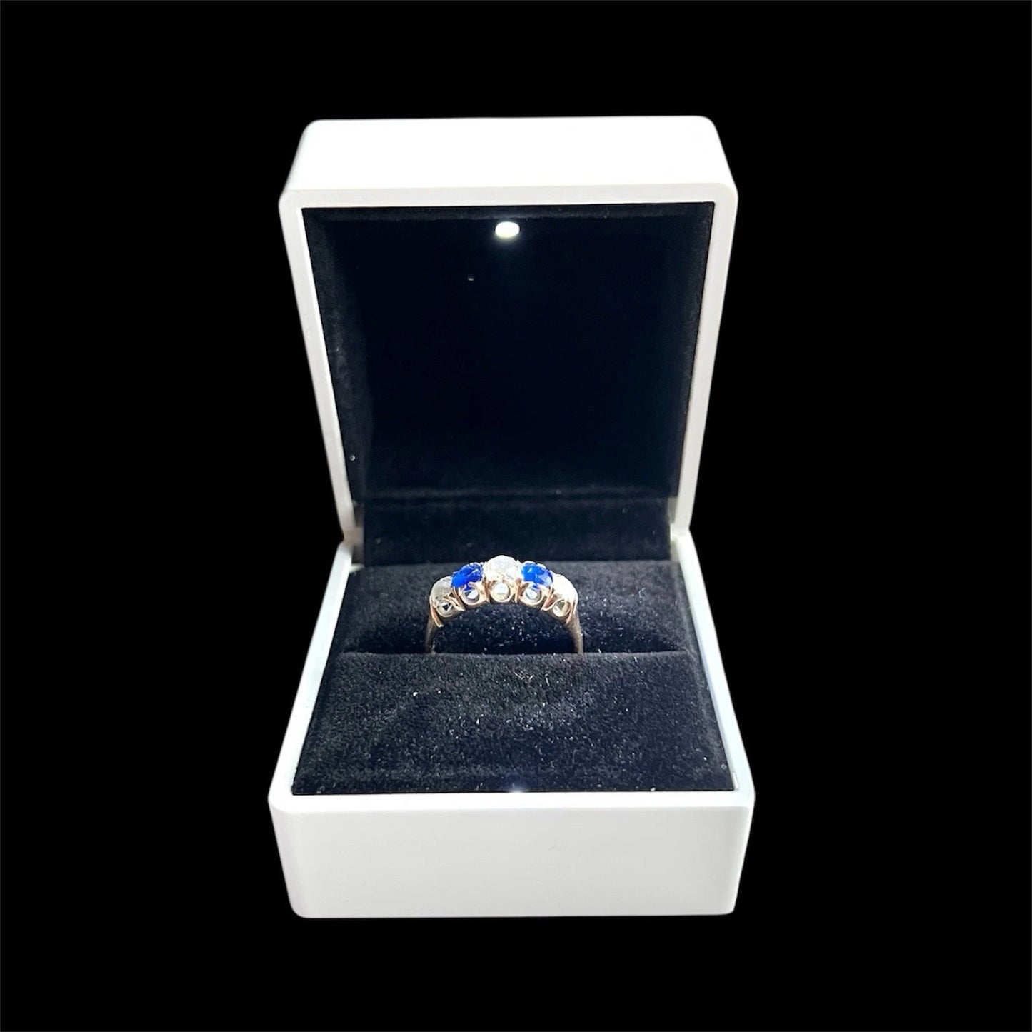 Ring with blue gemstones in a white box on a black background