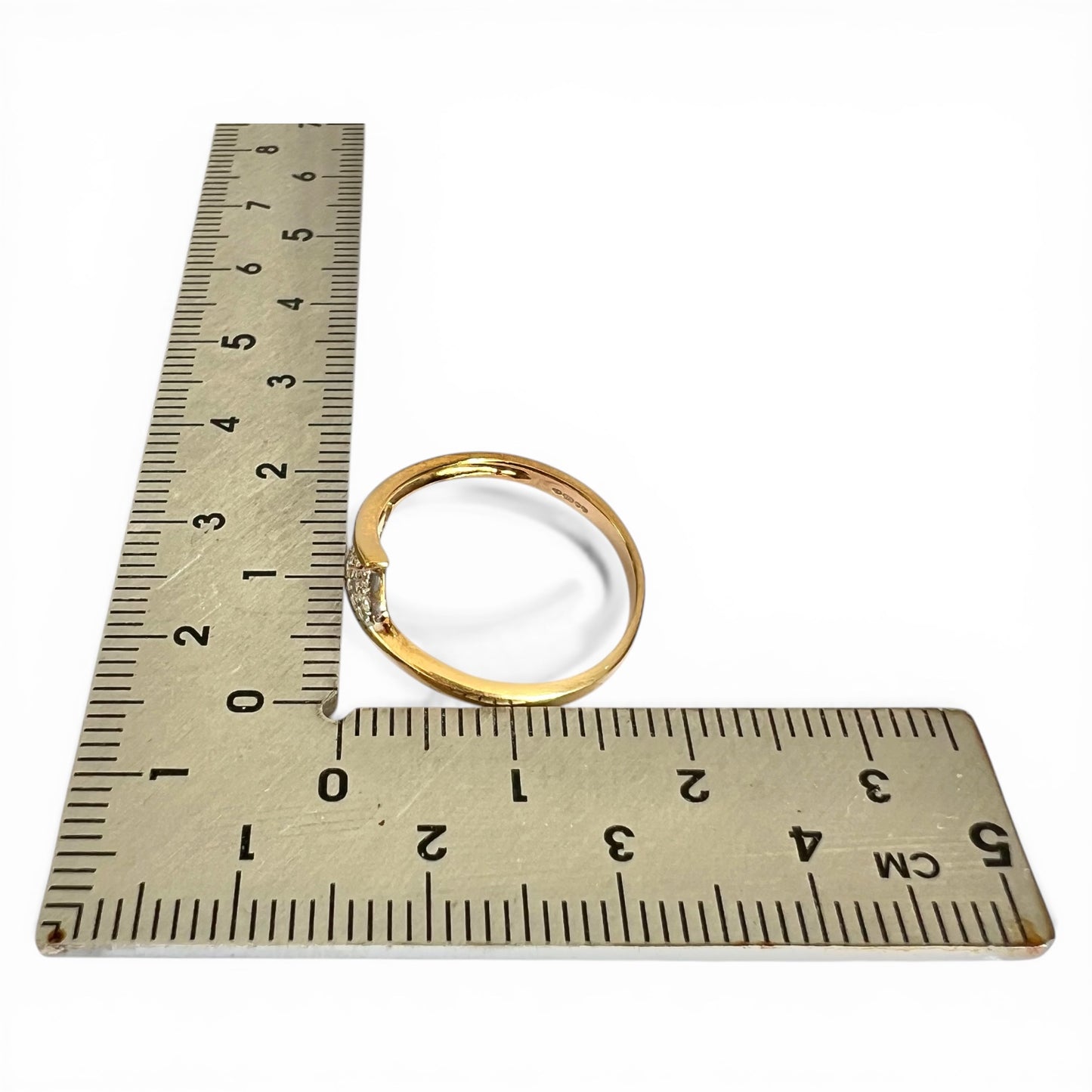 Gold ring next to a ruler on a white background
