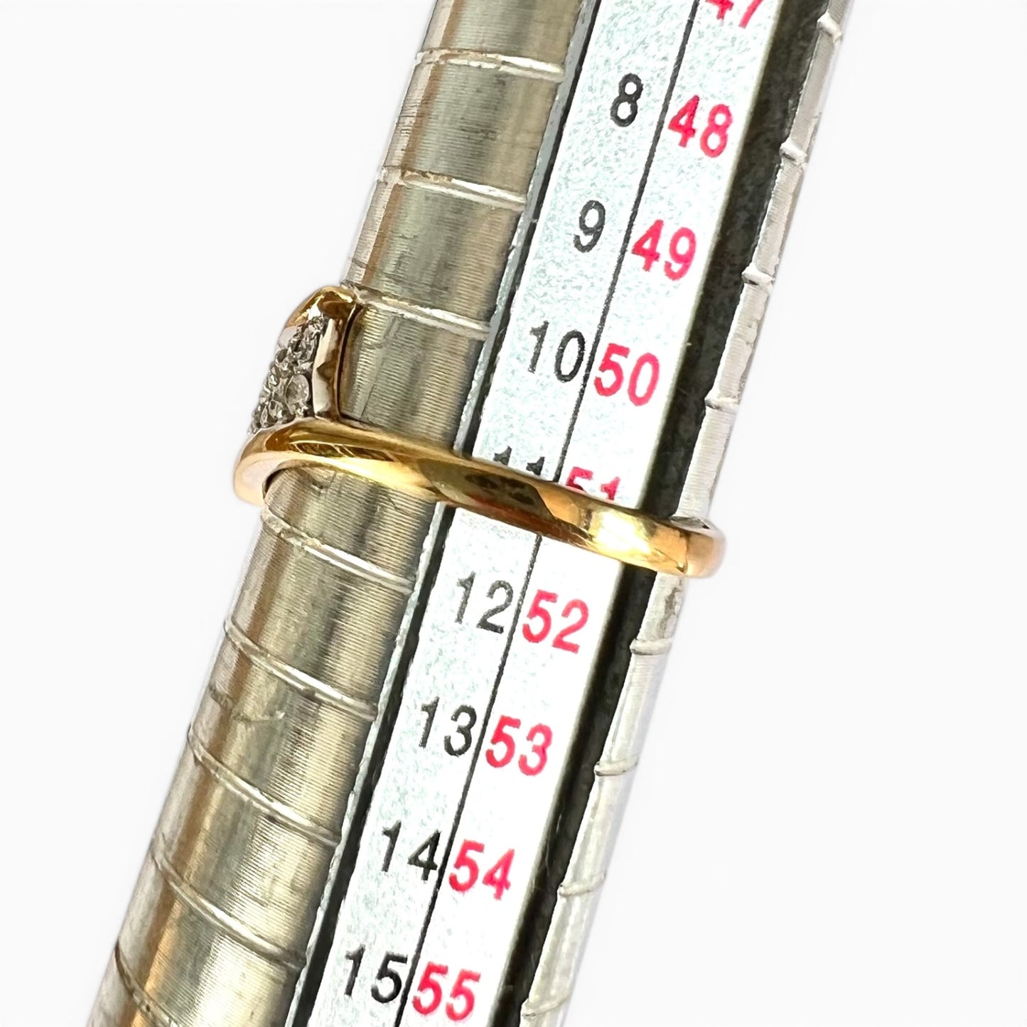 Gold ring being measured against a ruler on a white background