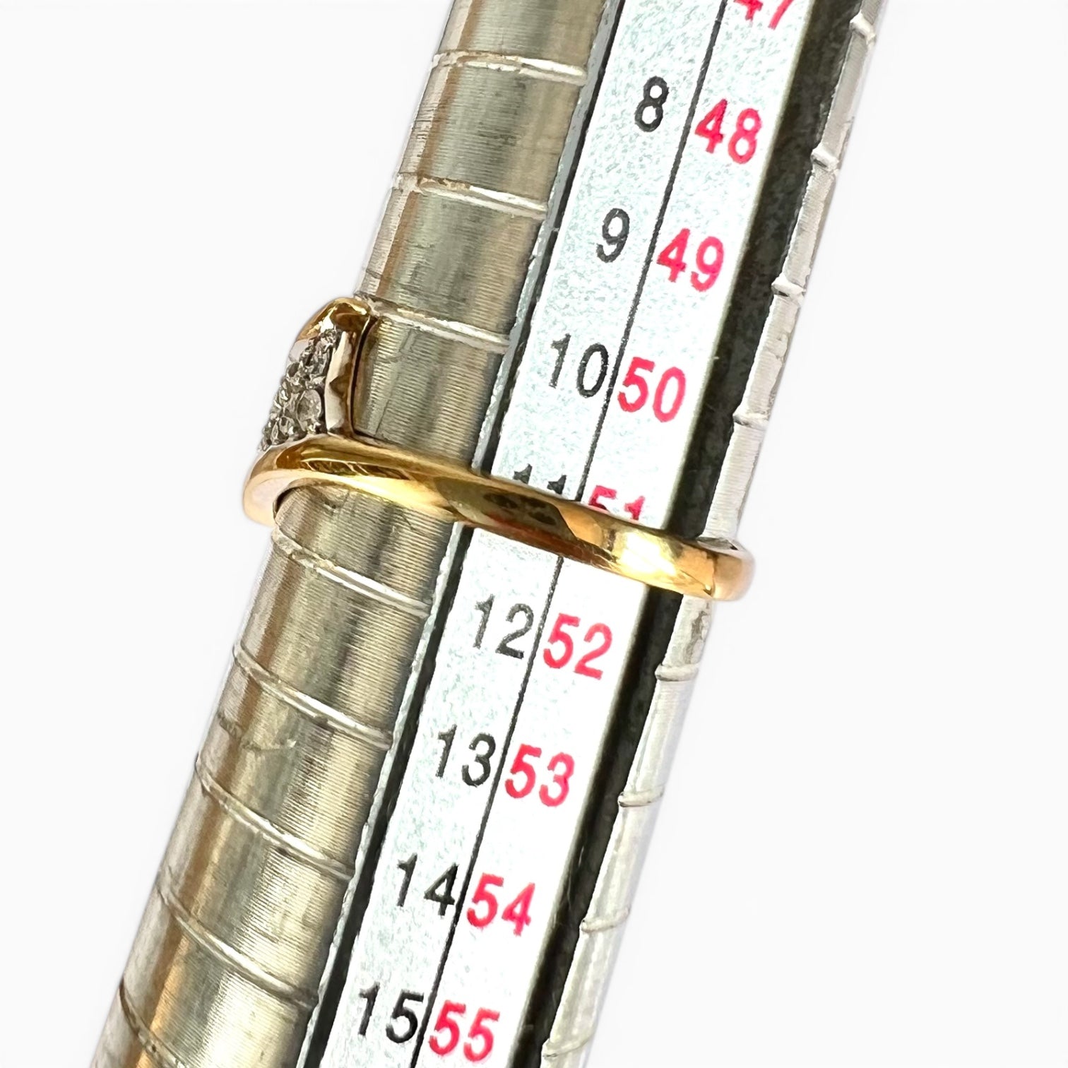 Gold ring being measured against a ruler on a white background