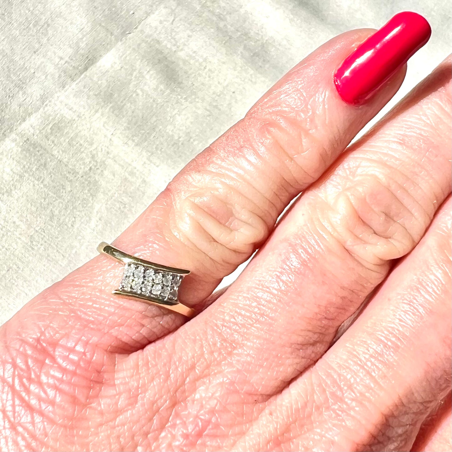 Gold ring with diamonds on a finger with pink nail polish against a light background