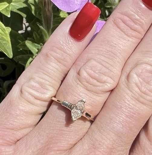 Hand wearing a marquise shaped yellow diamond ring with a blurred floral background